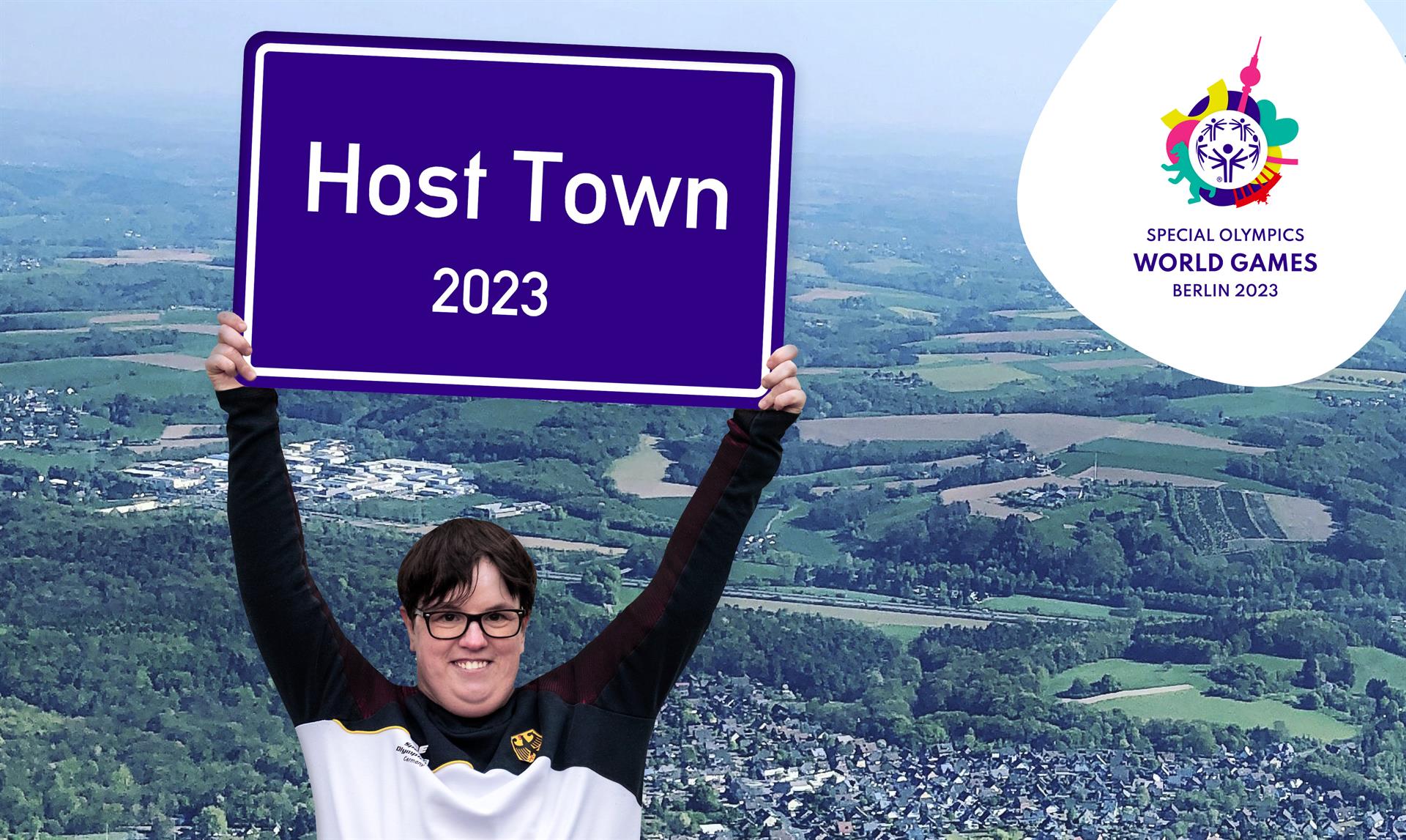 Frau hält Schild in den Händen mit der Beschriftung Host Town 2023