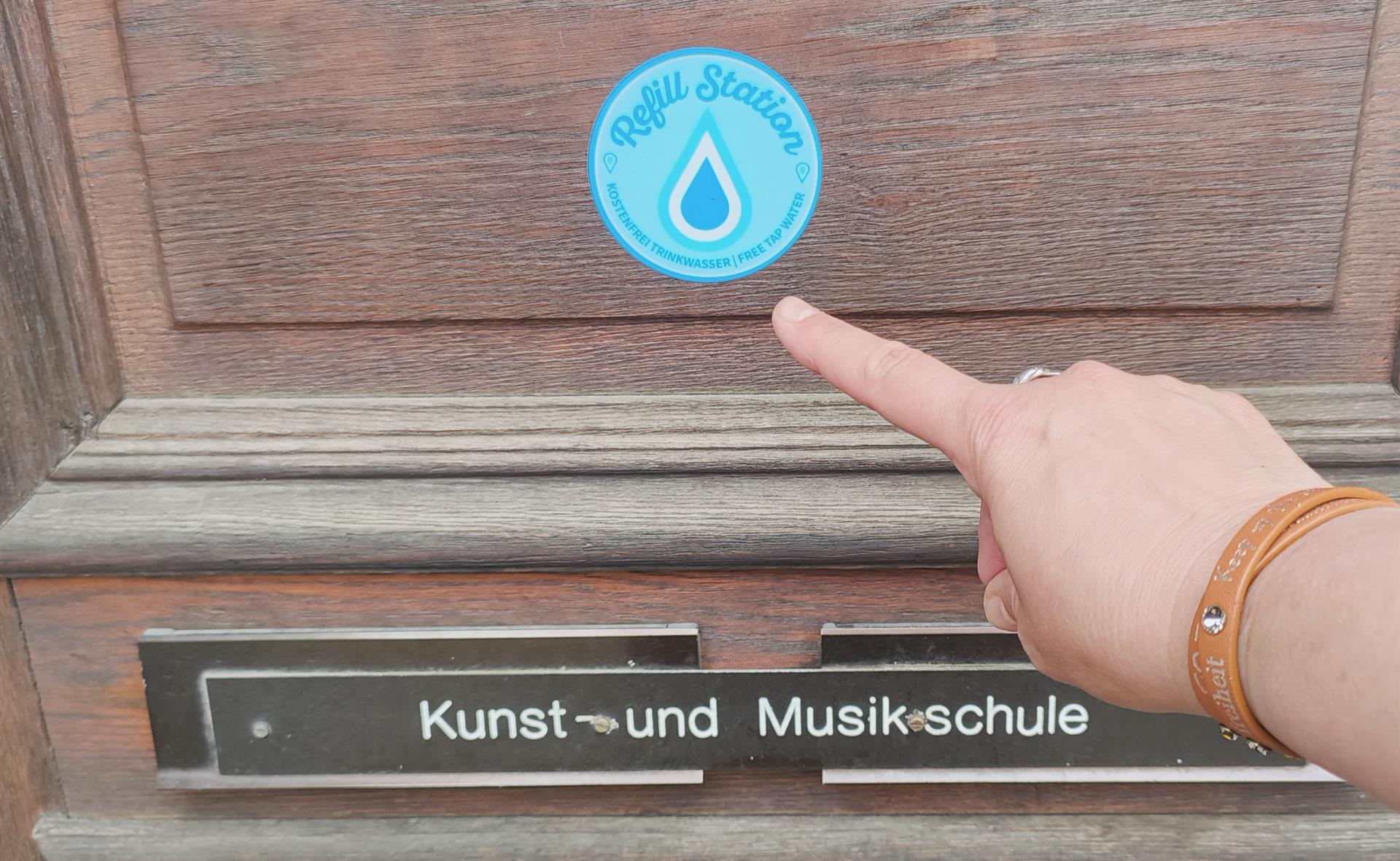 Das Bild zeigt einen blauen Aufkleber mit Wassertropfen in einem Kreis mit der Überschrift Refill Station an einer Eingangstür.